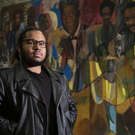 Tyler A. Ray stands in front of one of 14 murals inside the Church of the Advocate.