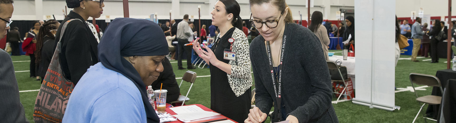 Two women speak to each other at a Temple job fair table.